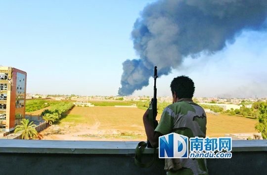 2日，利比亞首都的黎波里，一民兵武裝成員眺望被火箭彈擊中的儲油罐冒出濃煙。