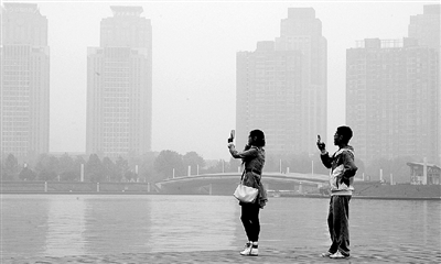 29日中午，鄭東新區(qū)如意湖畔，兩個(gè)年輕人拍攝霧霾中的景色。 鄭州晚報(bào)記者 馬健 圖