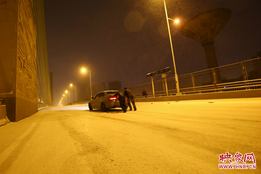 雪天路滑，汽車上橋打滑，兩名“推車人”幫助一輛私家車上坡。