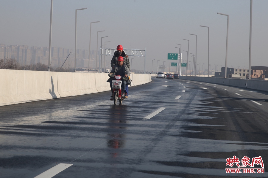 兩名工人騎車經(jīng)過灑水養(yǎng)護路面。